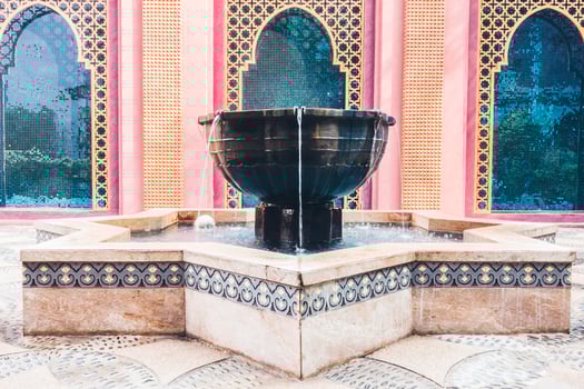 A fountain in a courtyard with a pink building in the background photo