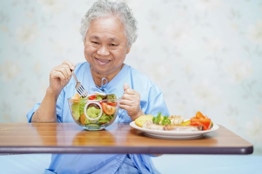 Asian elderly woman patient eating salmon stake and vegetable salad for healthy food in hospital. photo