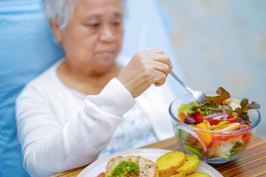 Asian elderly woman patient eating salmon stake and vegetable salad for healthy food in hospital. photo