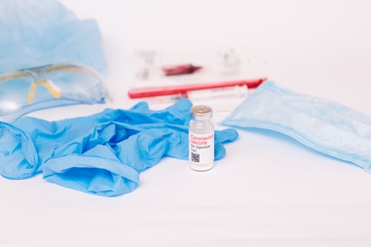 Coronavirus vaccine. Medical preparation in ampoule. Treatment for the disease, covid-19. The vaccine on a white background and on the background of a syringe, rubber gloves and goggles photo