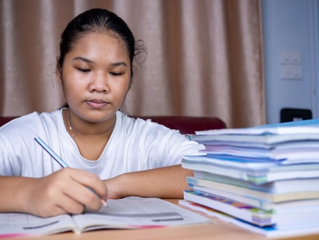 girl doing homework on a wooden table and there was a pile of books next to it The background is a red sofa and cream curtains. photo
