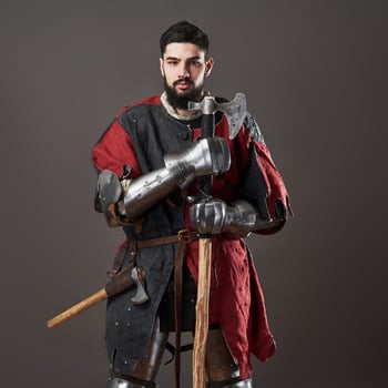 Medieval knight on grey background. Portrait of brutal dirty face warrior with chain mail armour red and black clothes and battle axe photo