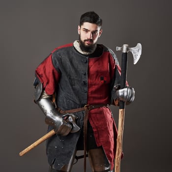 Medieval knight on grey background. Portrait of brutal dirty face warrior with chain mail armour red and black clothes and battle axe photo
