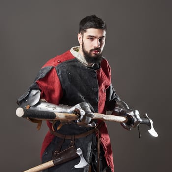 Medieval knight on grey background. Portrait of brutal dirty face warrior with chain mail armour red and black clothes and battle axe photo