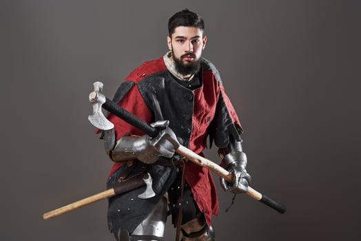 Medieval knight on grey background. Portrait of brutal dirty face warrior with chain mail armour red and black clothes and battle axe photo