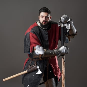 Medieval knight on grey background. Portrait of brutal dirty face warrior with chain mail armour red and black clothes and battle axe photo