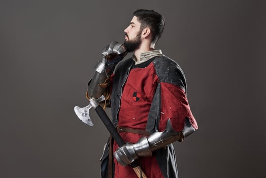 Medieval knight on grey background. Portrait of brutal dirty face warrior with chain mail armour red and black clothes and battle axe photo