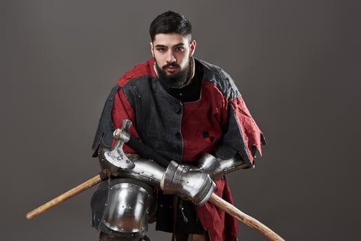 Medieval knight on grey background. Portrait of brutal dirty face warrior with chain mail armour red and black clothes and battle axe photo