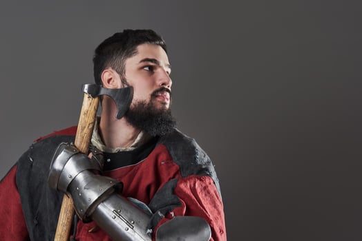 Medieval knight on grey background. Portrait of brutal dirty face warrior with chain mail armour red and black clothes and battle axe photo