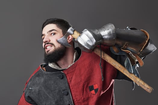 Medieval knight on grey background. Portrait of brutal dirty face warrior with chain mail armour red and black clothes and battle axe photo