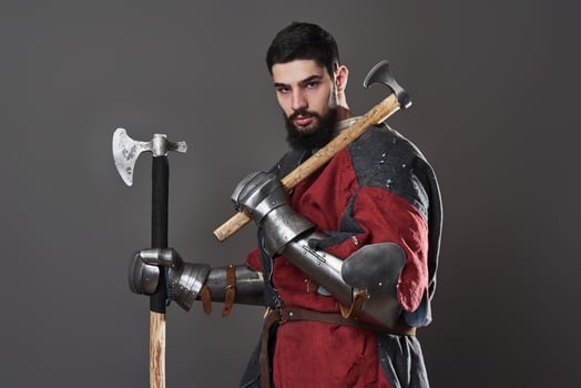 Medieval knight on grey background. Portrait of brutal dirty face warrior with chain mail armour red and black clothes and battle axe photo