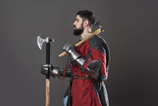 Medieval knight on grey background. Portrait of brutal dirty face warrior with chain mail armour red and black clothes and battle axe photo