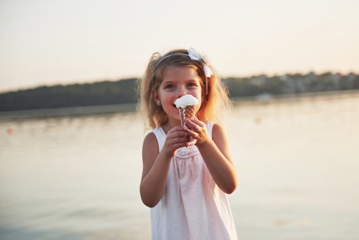 A beautiful little girl eats an ice cream near the water photo