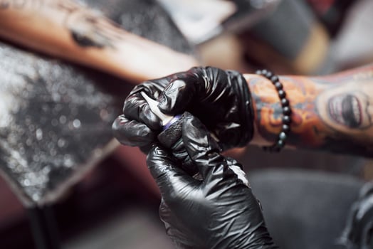 Close up tattoo machine. Master in black sterile gloves creating picture on hand with it in salon photo