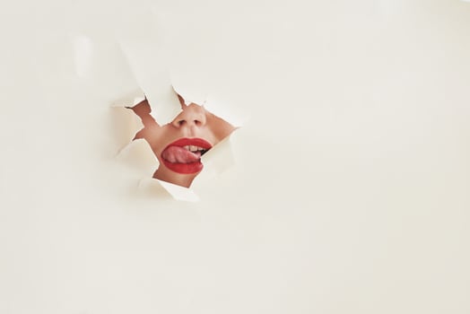 Licks her own lips. Torn hole in white paper with mouth of young woman photo
