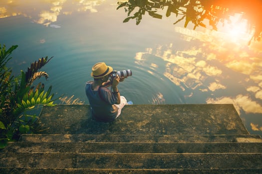 hipster man taking a photograph on pier against beautiful skies reflect on lake photo