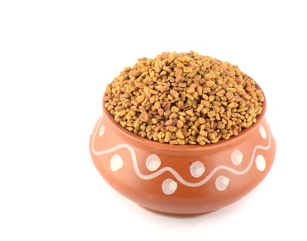 Fenugreek seeds in clay pot isolated on white background photo