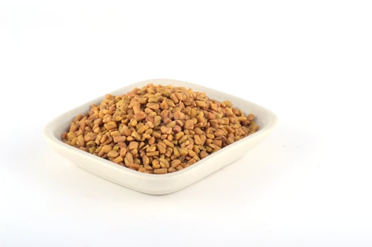 Fenugreek seeds in white plate isolated on white background photo