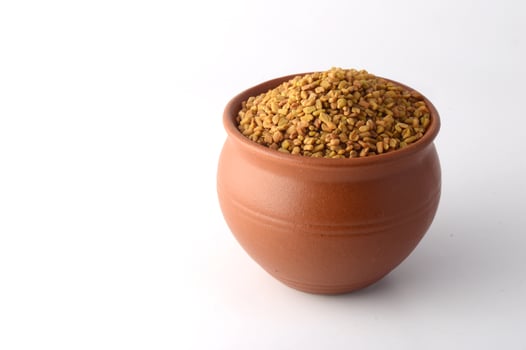 Fenugreek seeds in clay pot isolated on white background photo