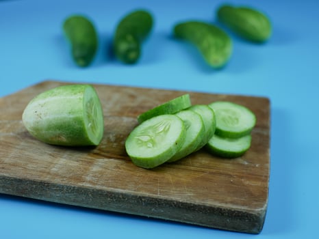 sliced cucumber on wooden cutting board with a blue background. healthy diet food concept photo