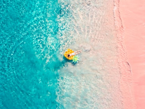 Drone aerial view of girl floating on inflatable pineapple at exotic tropical pink beach photo