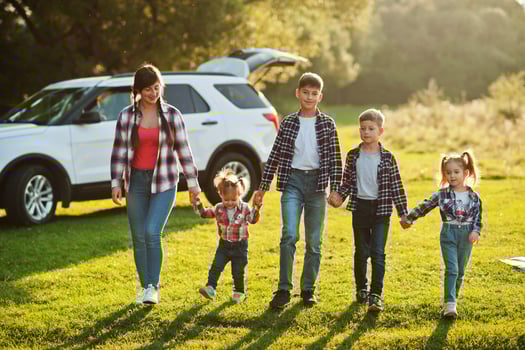Family spending time together. Mother with four kids standing and holding hands against white suv car. photo