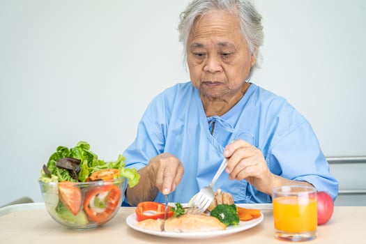 Asian senior or elderly old lady woman patient eating Salmon steak breakfast with vegetable healthy food while sitting and hungry on bed in hospital. photo