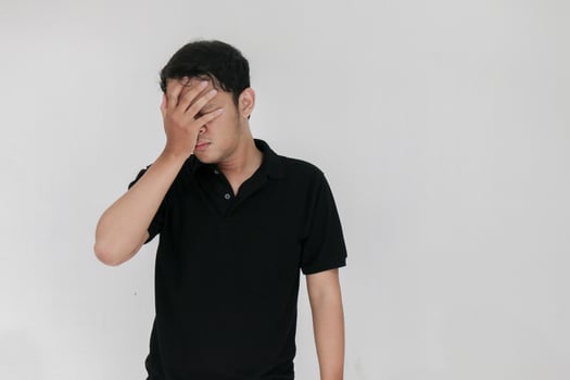 Portrait of young asian man isolated on grey background suffering from severe headache, pressing fingers to temples, closing eyes to relieve pain with helpless face expression photo
