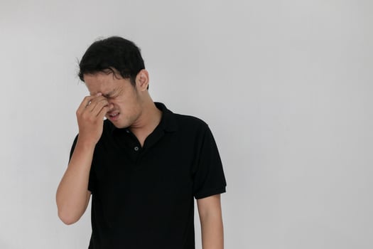 Portrait of young asian man isolated on grey background suffering from severe headache, pressing fingers to temples, closing eyes to relieve pain with helpless face expression photo