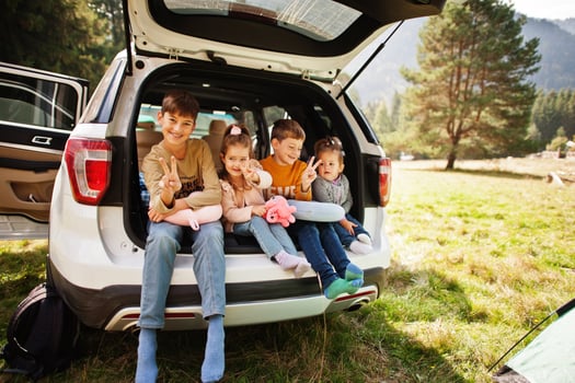 Family of four kids at vehicle interior. Children sitting in trunk. Traveling by car in the mountains, atmosphere concept. photo