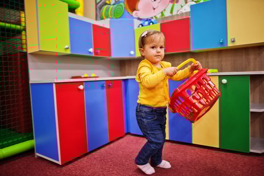 Cute baby girl playing in indoor play center. Kindergarten or preschool play room. Holds a basket for groceries in the children's kitchen. photo