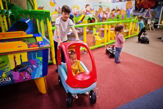 Four kids playing in indoor play center. Kindergarten or preschool play room. Riding toy car. photo