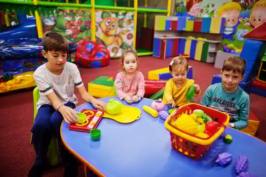 Four kids  playing in indoor play center. Kindergarten or preschool play room. Sitting by the table with plastic fruits. photo