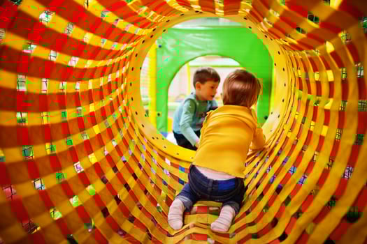 Kids playing in indoor play center. Kindergarten or preschool play room.  Baby girl climbs into the pipe. photo