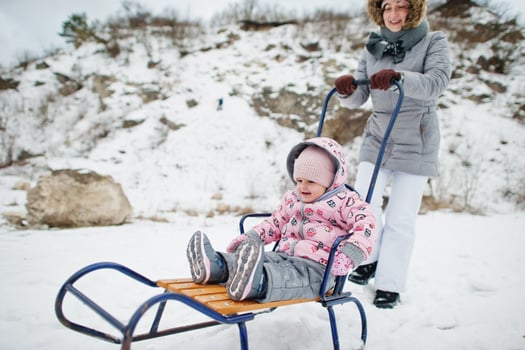 Mother and baby girl enjoy a sleigh ride. Child sledding. Kid riding a sledge on winter. photo