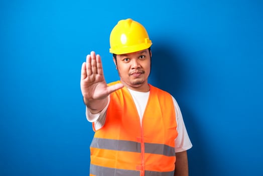 Fat asian workman wearing orange safety vest and yellow helmet making stop gesture photo