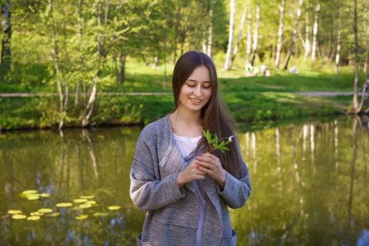 the girl stands against the background of the lake holding a flower in her hands photo