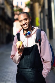 Young black man eating an apple walking down the street. photo