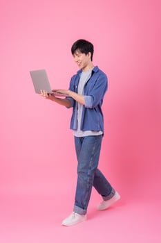 Young Asian man standing and using laptop on pink background photo