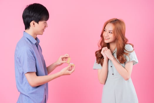 Young Asian man proposes to his girlfriend on a pink background photo