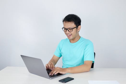 Young Asian man feeling happy and smile when work laptop on table. Indonesian man wearing blue shirt. photo