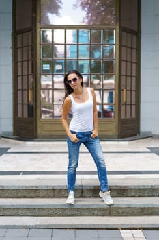 Cute woman in sunglasses poses on the steps in the street near the building photo