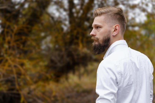 Young bearded man in white shirt walks on yellow autumn day in park. Spending photo
