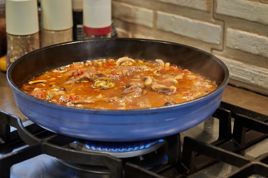 Veal tongue with tomato sauce, mushrooms and capers is fried in frying pan on gas stove. French gourmet cuisine photo
