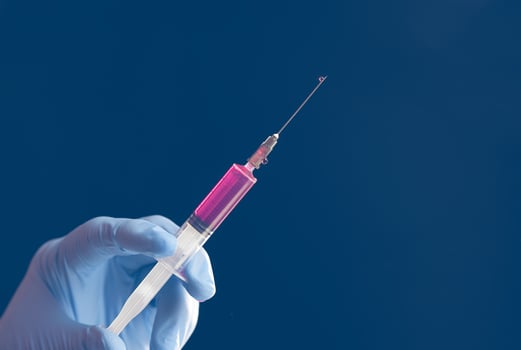 Doctor's blue-gloved hand holding a syringe with red liquid isolated on blue background. photo