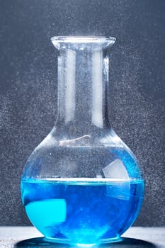 Glass flask with a blue liquid on gray background. photo