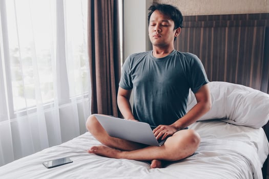 Work from home. Young asian man sits on a bed. Home workplace. Break, relaxation at the time of work. photo