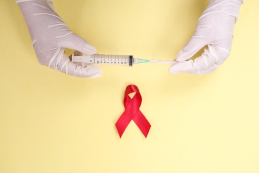 red ribbon with medical gloves and syringe against HIV isolated on yellow background photo