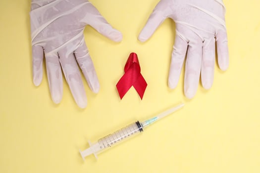 red ribbon with medical gloves and syringe against HIV isolated on yellow background photo
