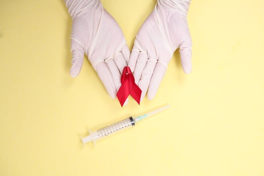 red ribbon with medical gloves and syringe against HIV isolated on yellow background photo